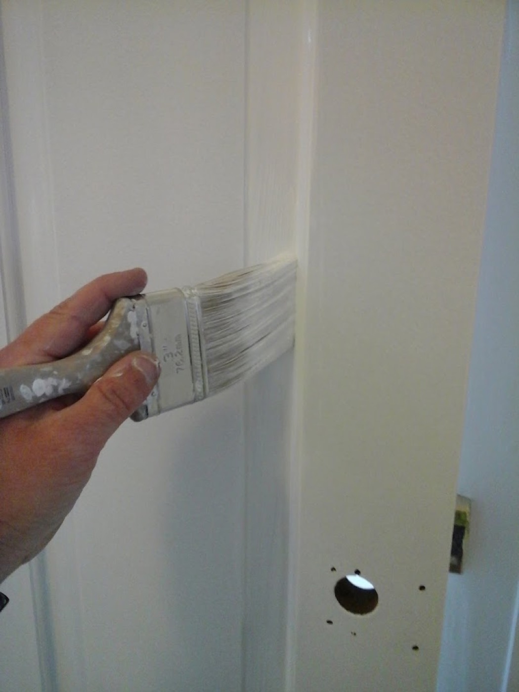 A hand cutting in the edge of a white internal door with a paintbrush