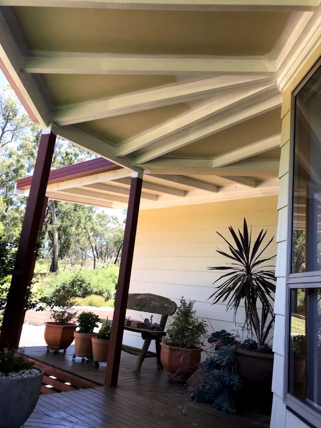 A finished verandah with painted posts, potted plants and a timber deck