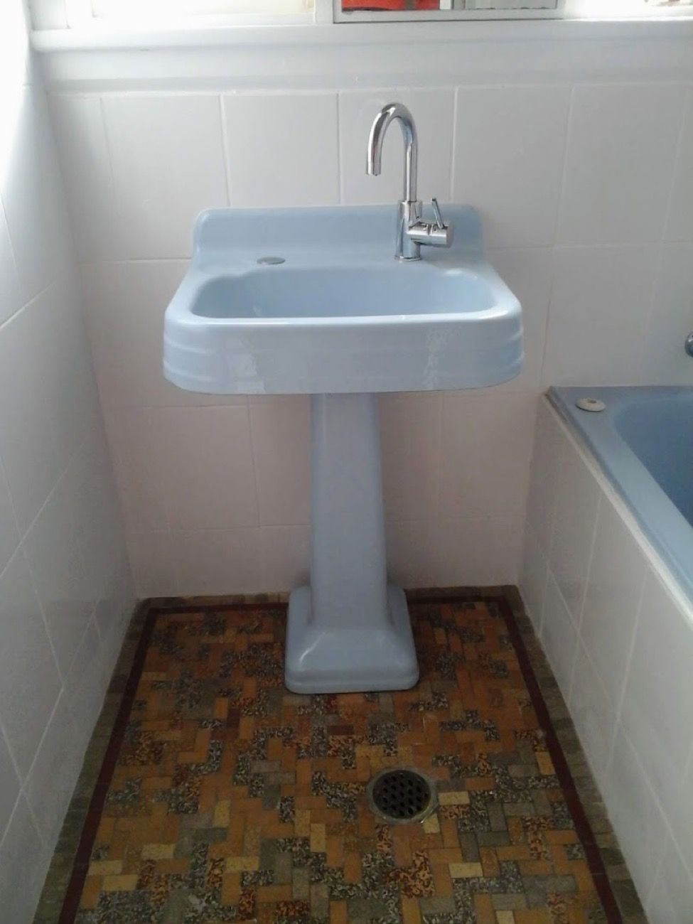 A bathroom with a pedestal basin, tiled floor and a bath alongside