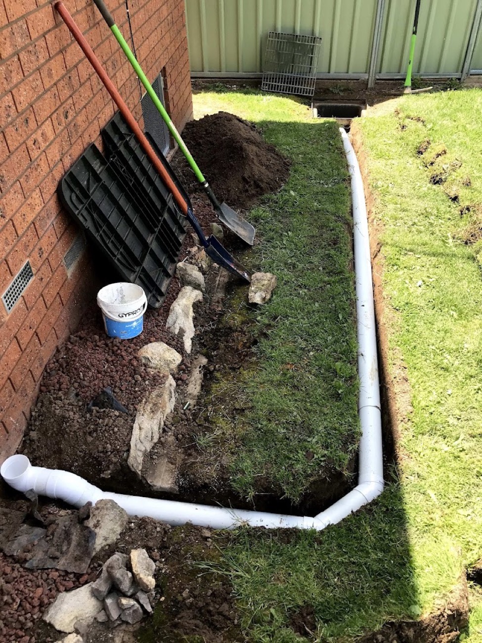 A trench dug along a lawn with new stormwater pipe laid into it