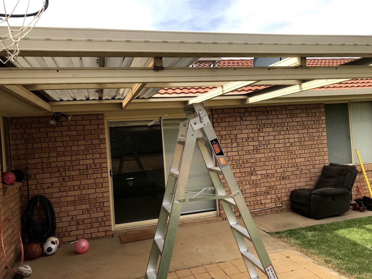 A pergola frame going up against a brick house with a ladder set against it