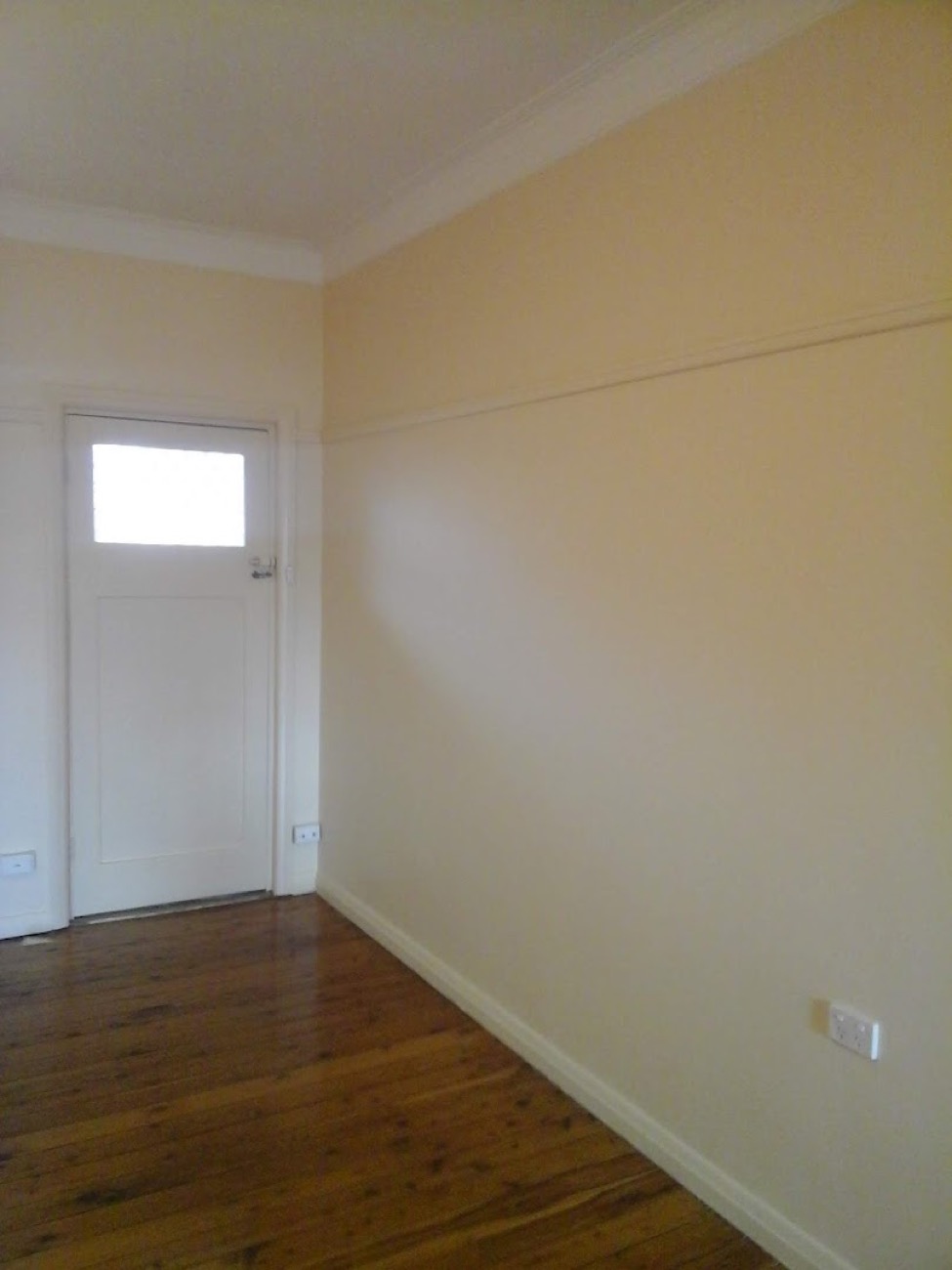 A repainted interior room with a white door and bare floorboards