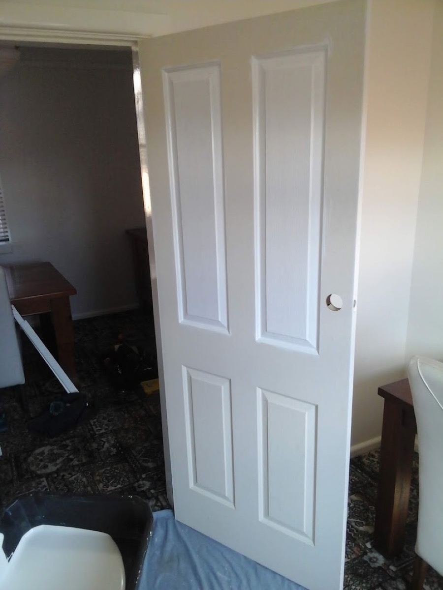 A new white panel door standing in its frame with a drop sheet on the floor