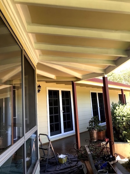 A patio roof on painted posts over a paved outdoor area