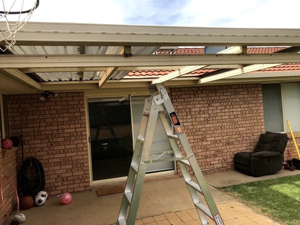 A patio frame going up against a brick house with a ladder alongside