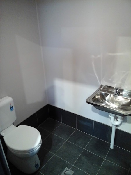A bathroom with a wall-hung basin and a toilet suite on dark tiles