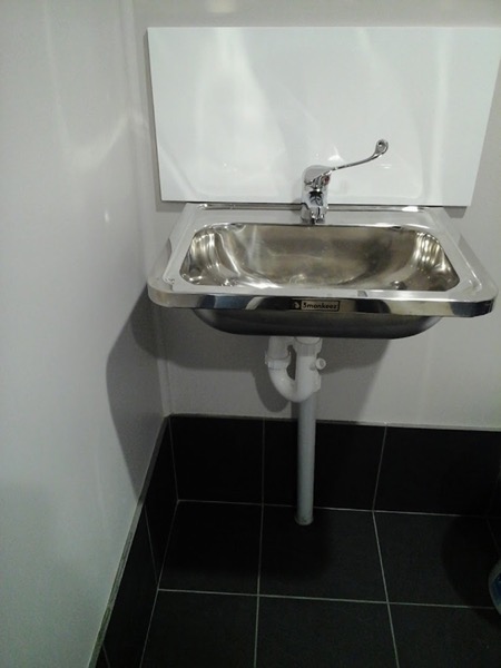 A stainless steel wall basin mounted above dark floor tiles