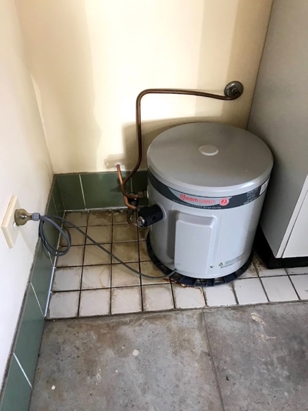 A hot water unit in a tiled corner with copper pipework