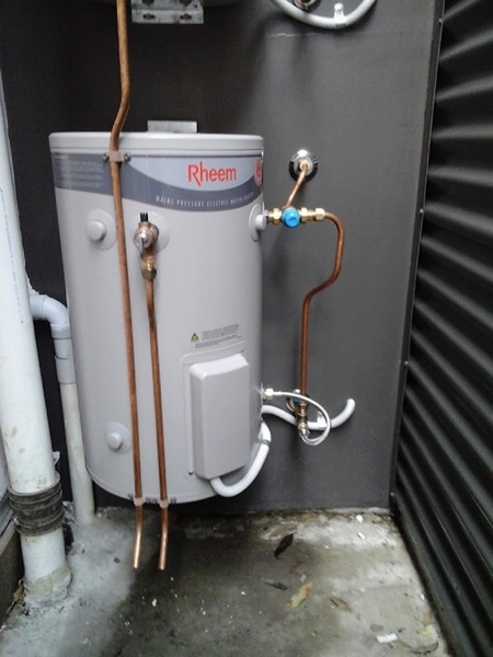 A hot water cylinder standing against a corrugated wall