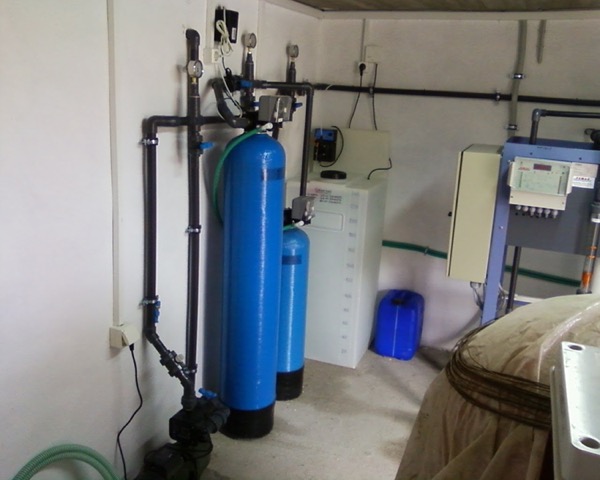 A wall-mounted filtration and pump setup with blue pressure vessels