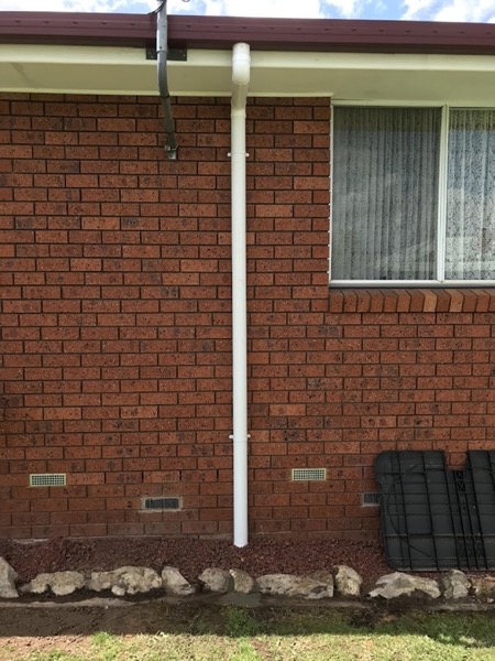 A downpipe against a brick wall with lengths of pipe stacked nearby