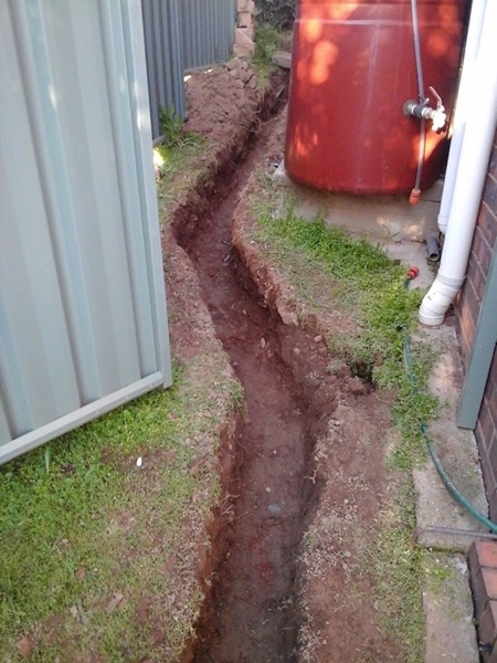 A trench dug along a fence line beside a water tank