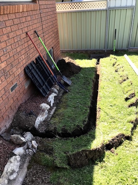 A trench along a brick wall with pipe laid in and rock backfill