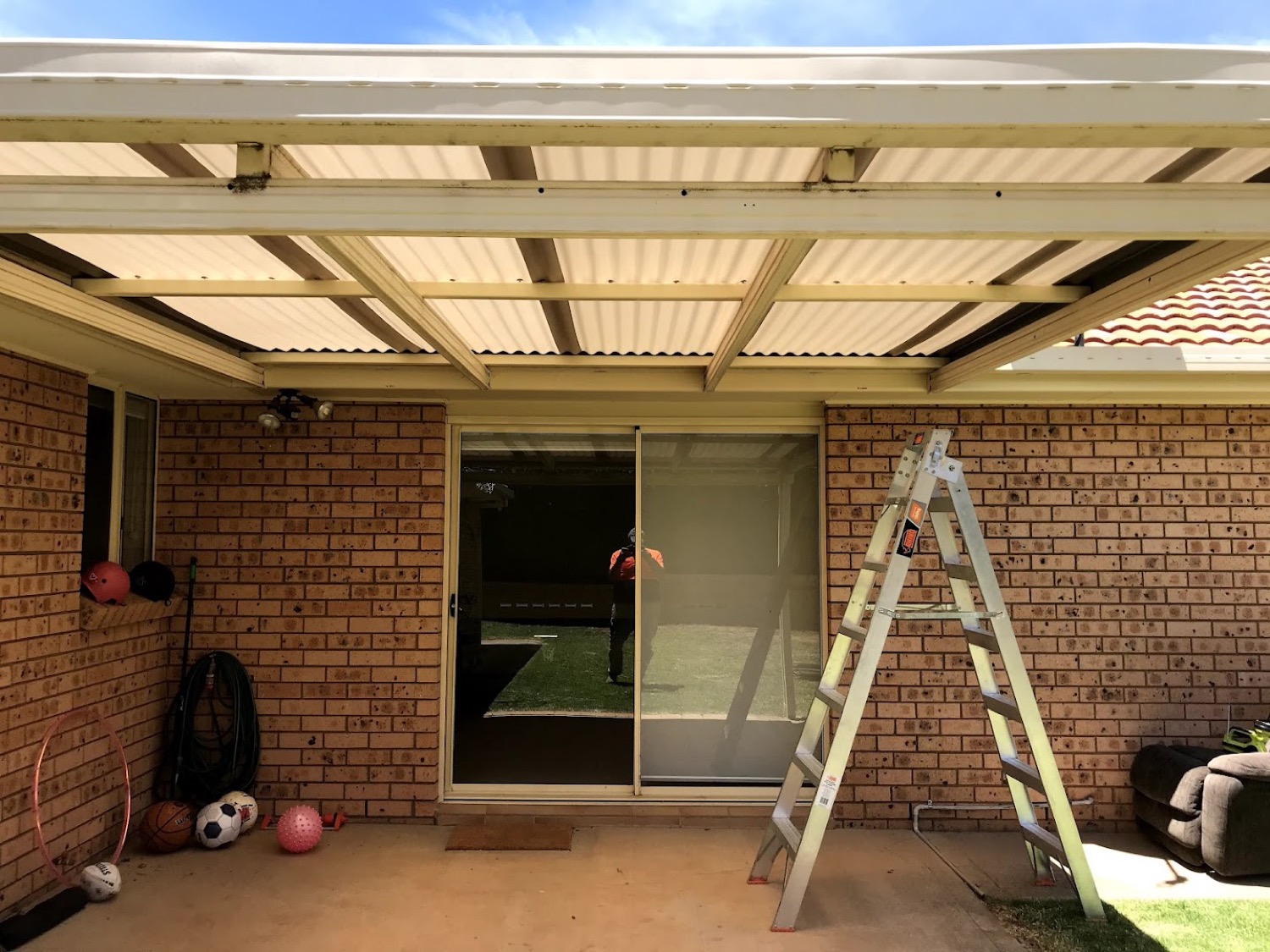 A timber pergola frame under construction beside a brick wall with a ladder alongside